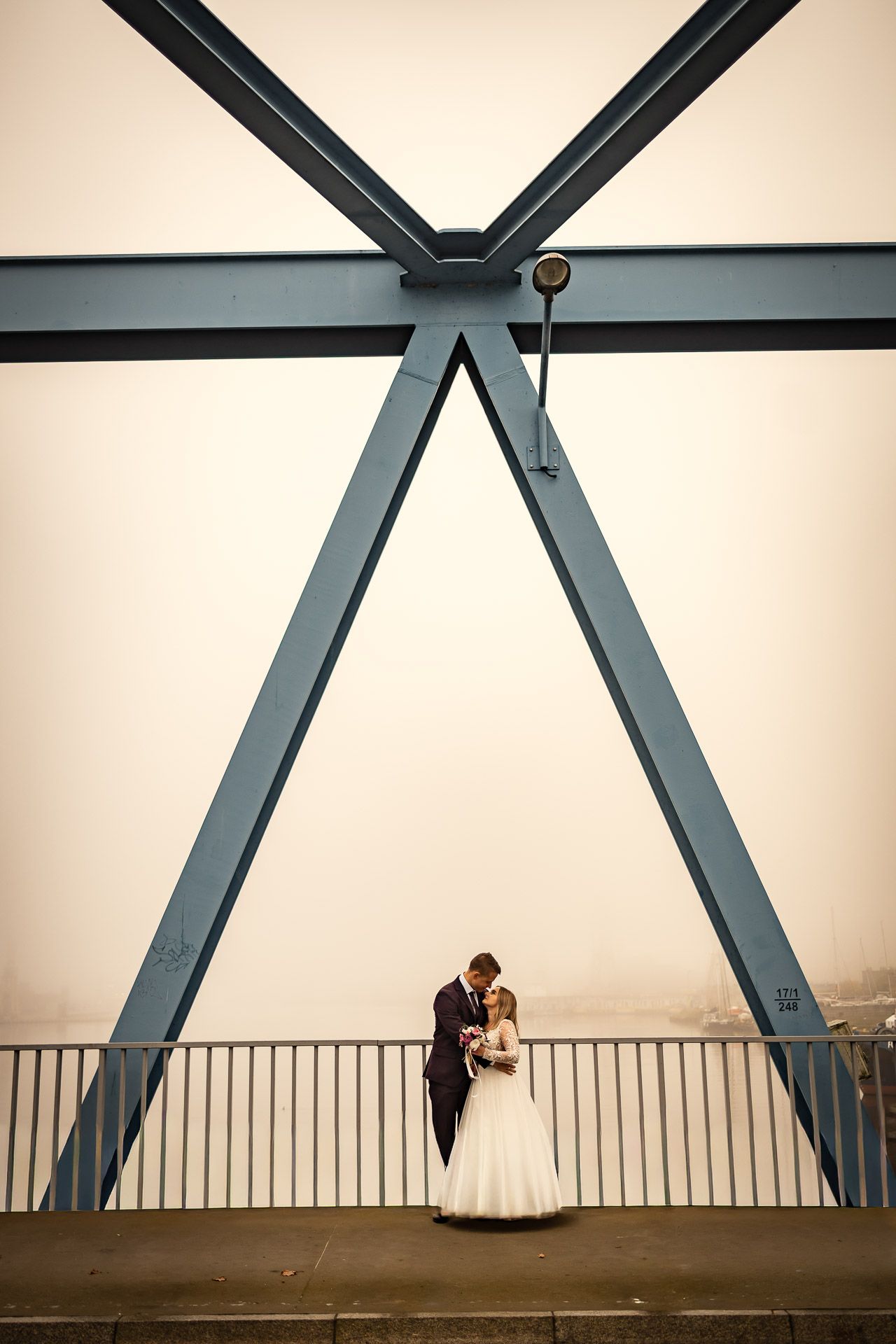 A wedding couple embraces beneath dramatic steel architecture.