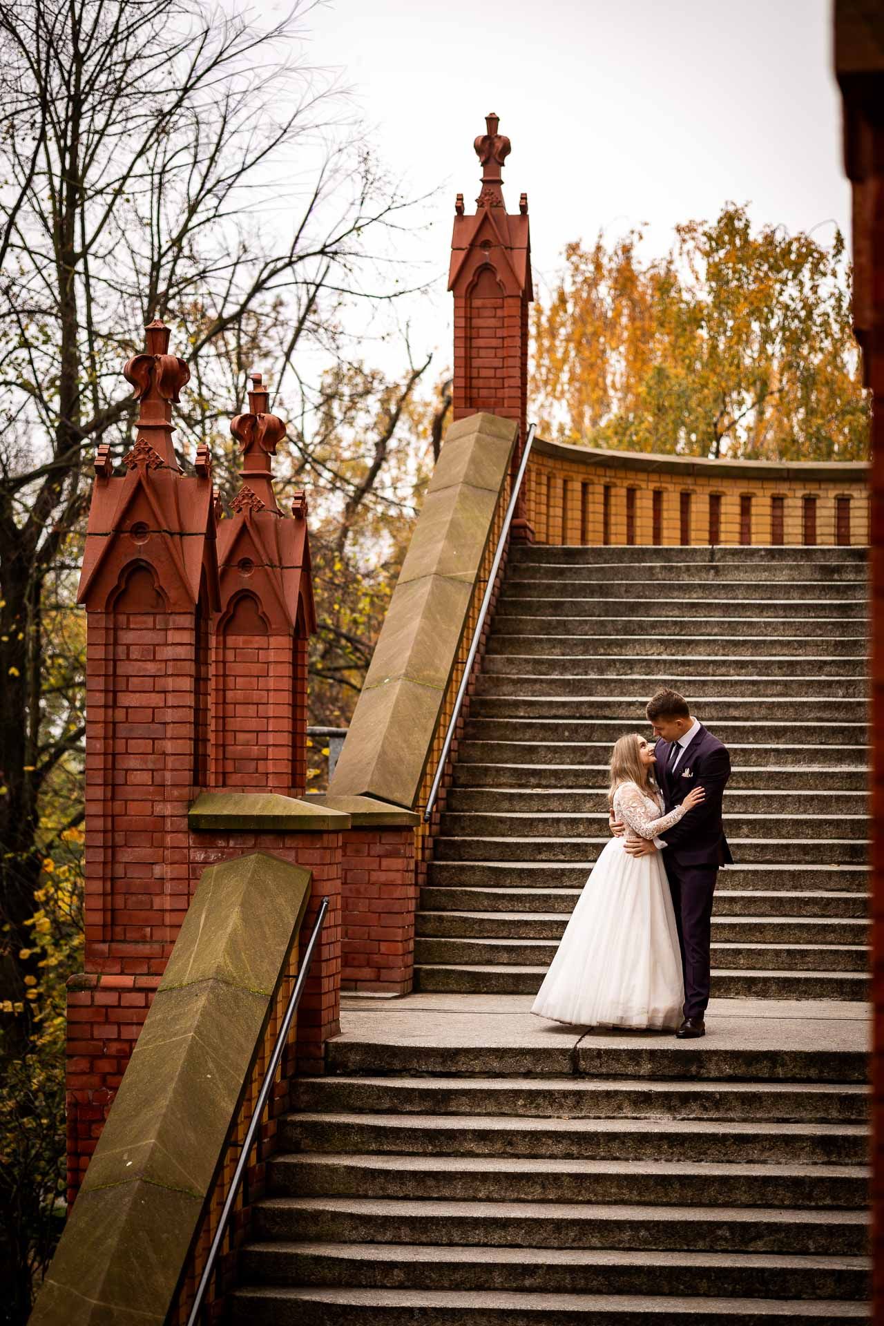 A wedding couple shares a romantic moment on ornate brick stairs.