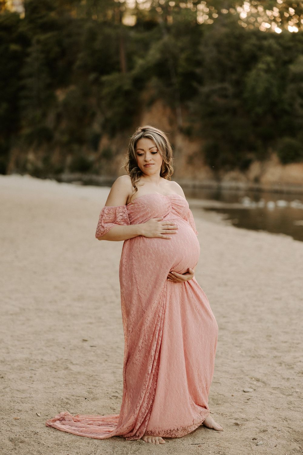 A person in a flowing pink lace dress sits peacefully on sandy ground during golden hour.