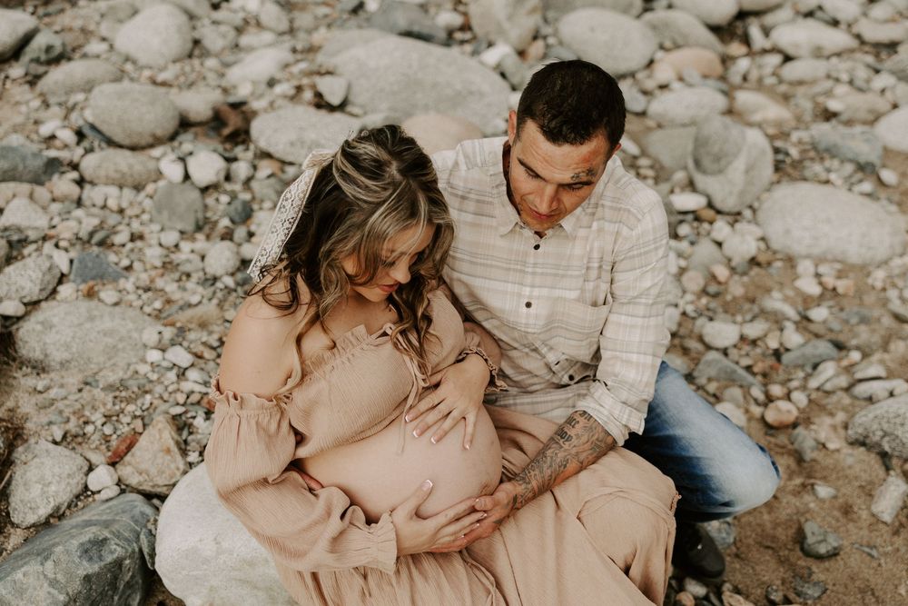 A couple sits together on rocky ground in warm earth tones during an intimate outdoor photo session.