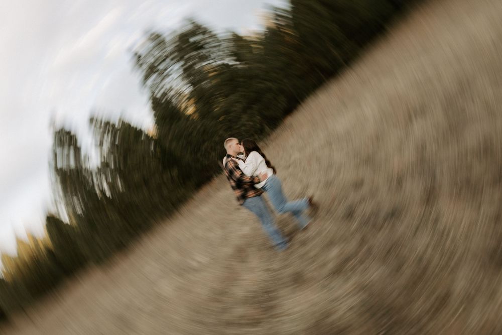 Motion blur photograph shows a skateboarder in jeans and white shirt riding on a tilted path outdoors.