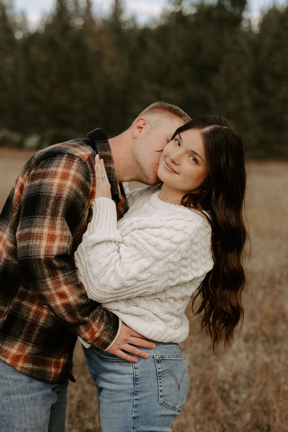 A couple in matching plaid and knit sweaters share romantic moments in a rustic autumn field setting.