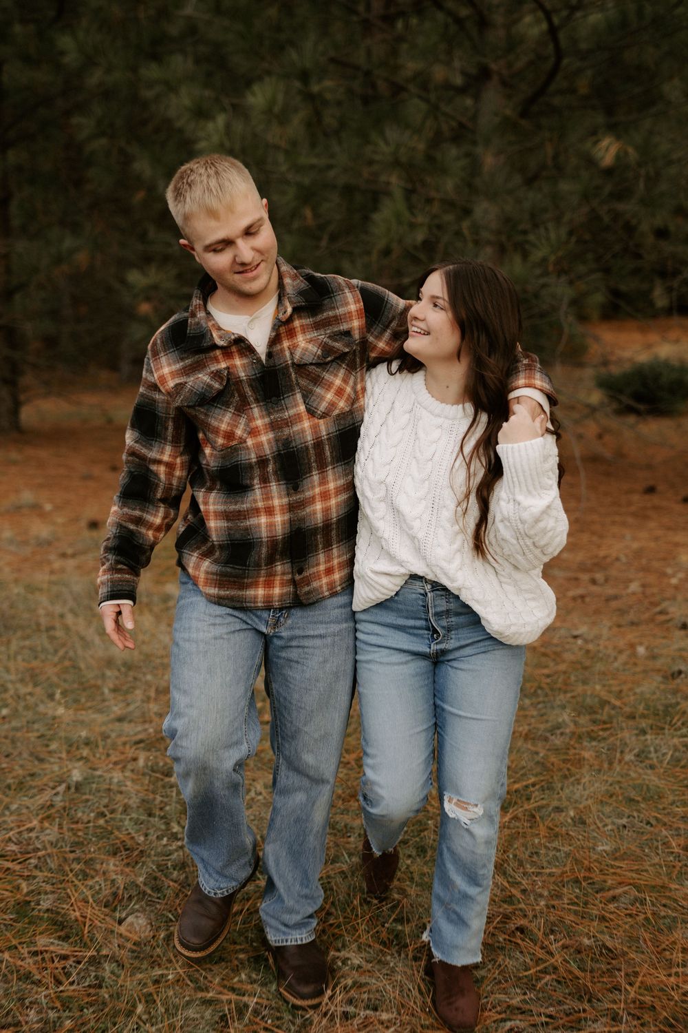 A couple wearing plaid and denim walk together through an autumn field sharing a candid laughing moment.