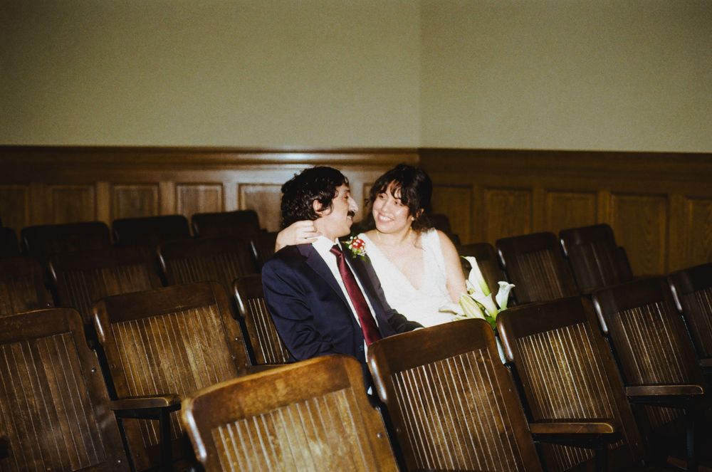 Couple sharing a romantic moment seated among wooden chairs in a vintage auditorium.