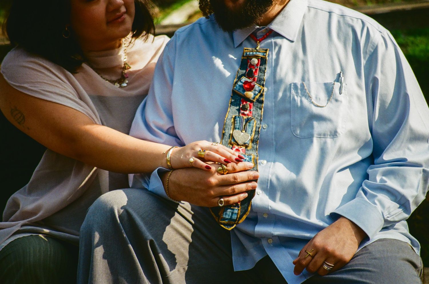 Close-up of couple holding hands, groom wearing a colorful novelty tie and blue shirt.