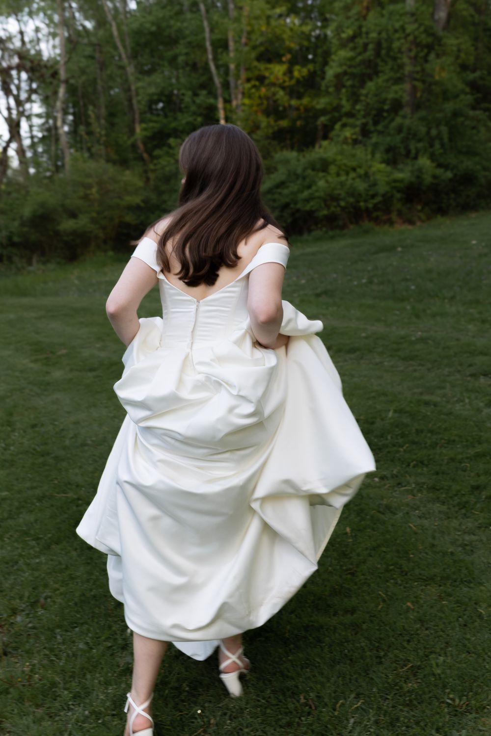 A person in a flowing white dress twirls gracefully on a grassy lawn surrounded by trees at dusk.