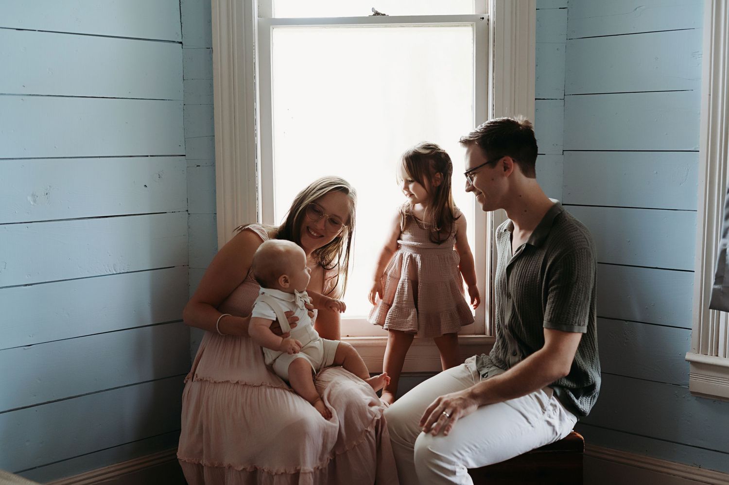 Family cuddling by the window of their home.