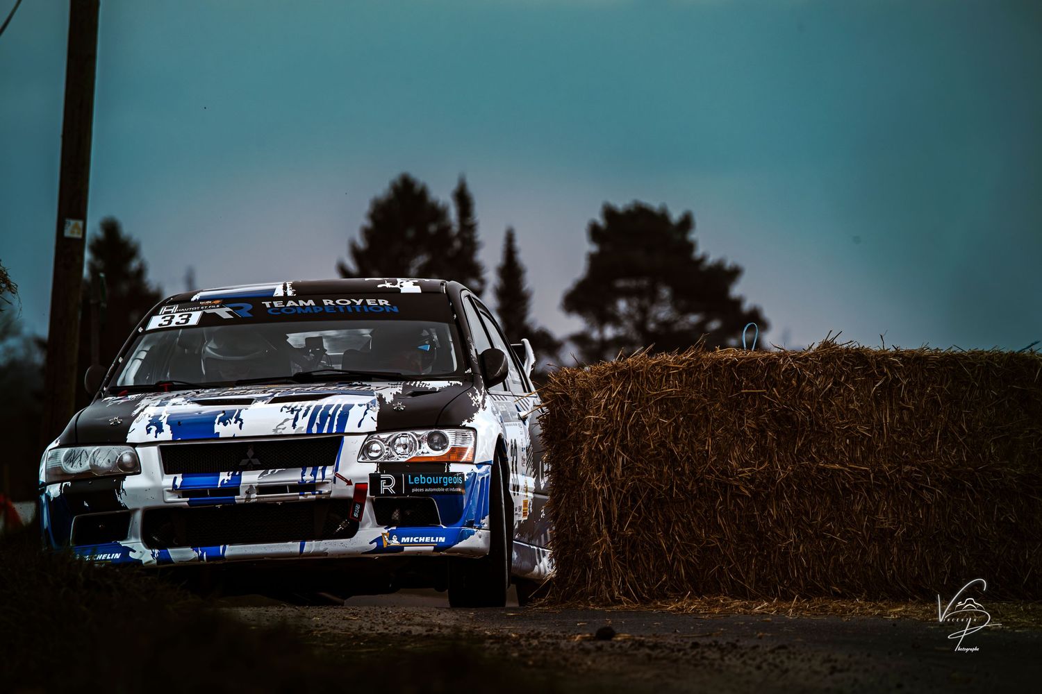 Rally cars racing through a scenic mountain course against blue sky.