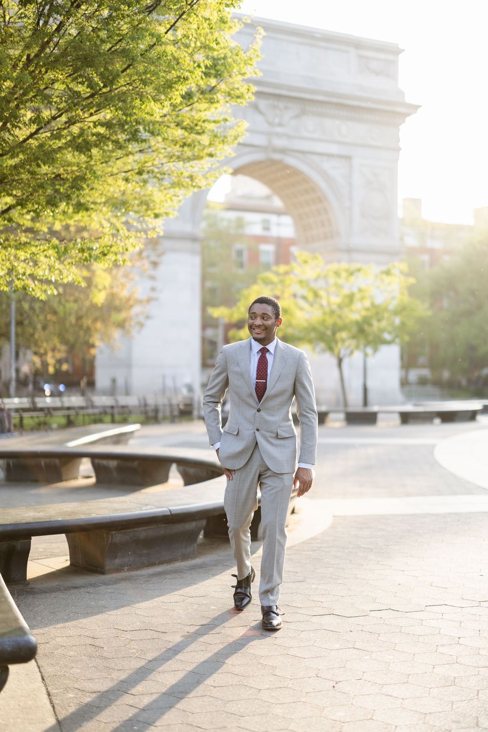Professional in a light suit walking confidently past Washington Square Arch on a sunny day.