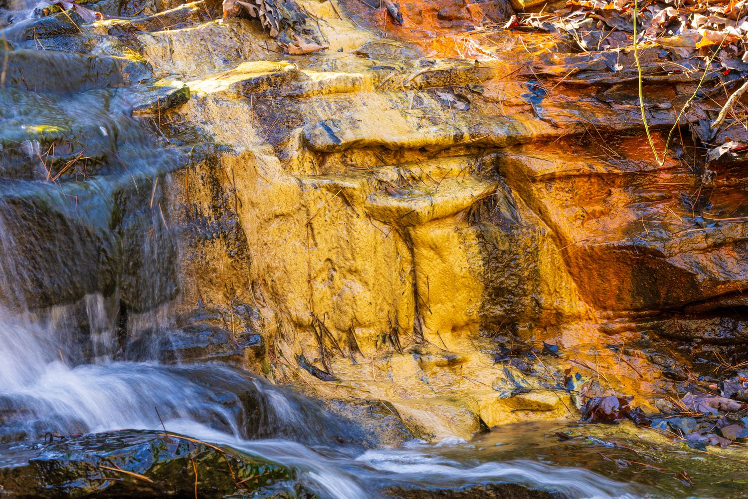 A scenic waterfall cascades over golden-lit rocky cliffs in a dramatic natural landscape at sunset.