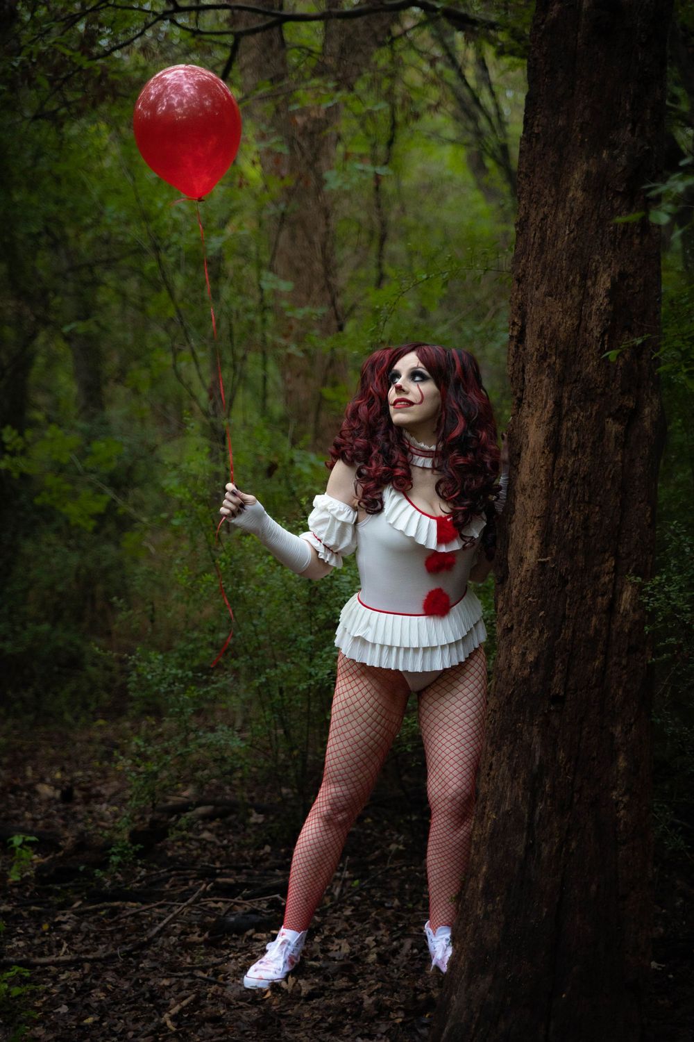 A woman dressed as IT poses in the woods with a red balloon.