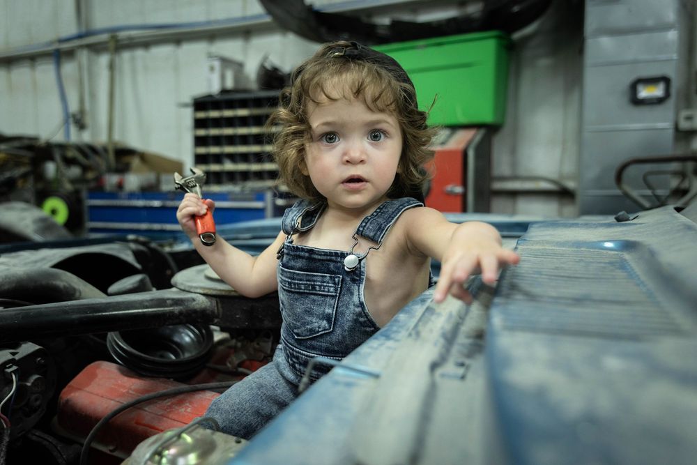 A young toddler poses in a car engine with a wrench.