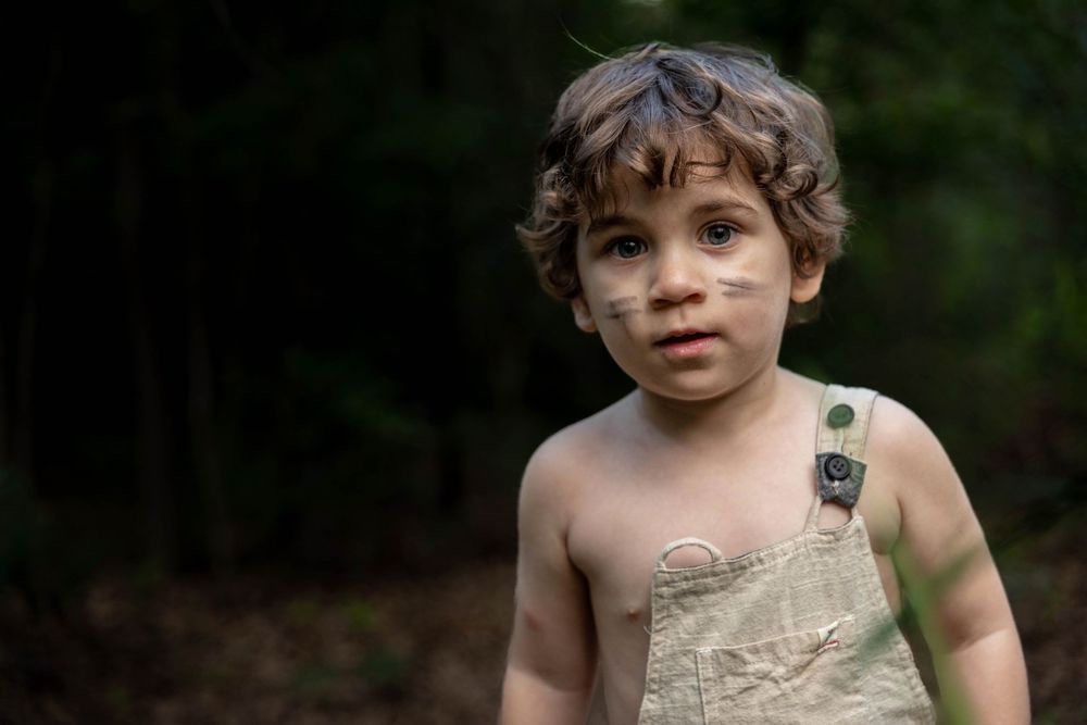 A boy pretending in a Peter Pan world poses for a photo in the woods.