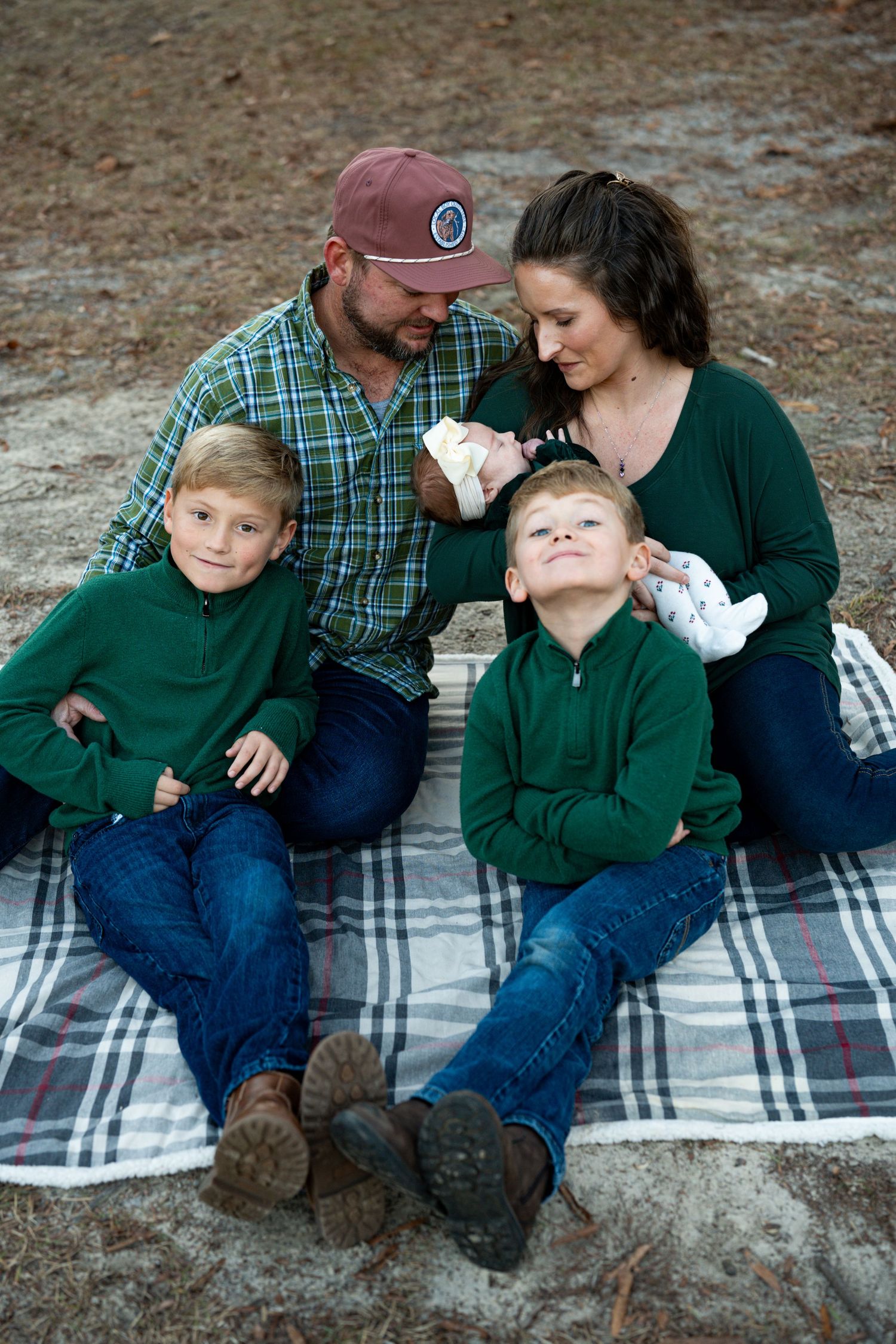 Two children in matching green sweaters sit together on a blanket during golden hour at sunset.