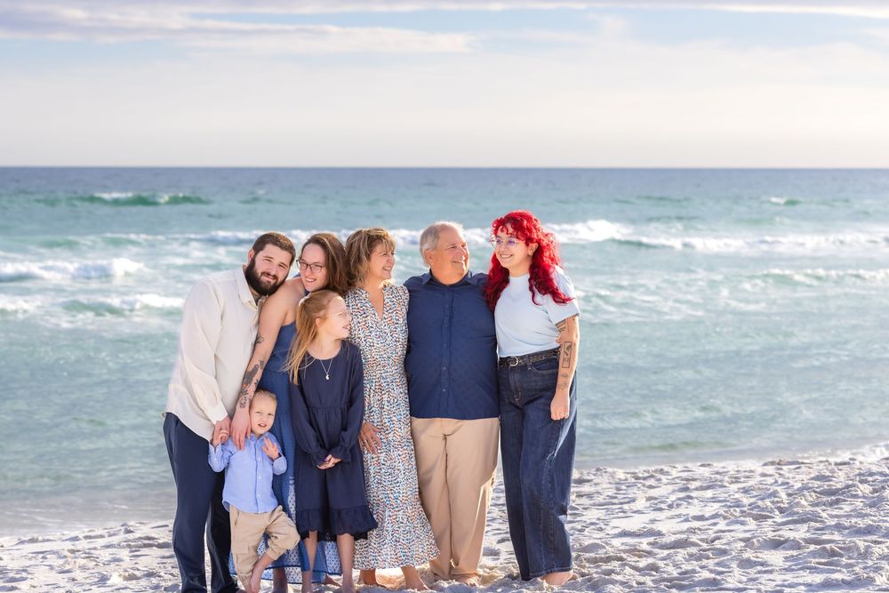 A family group poses together on a sunny beach with turquoise waves and white sand in the background.
