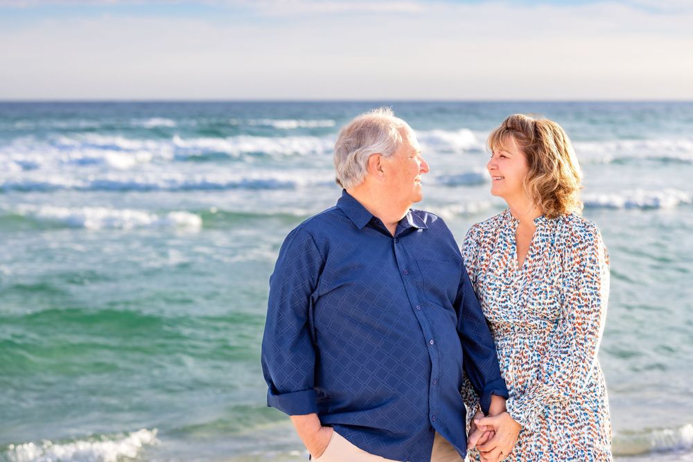 Romantic beach photoshoot featuring a couple in blue and patterned outfits by the ocean.
