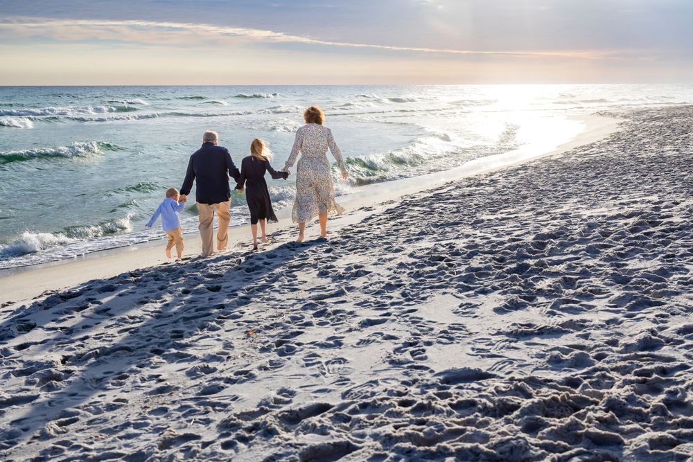 Three people walk hand in hand along a beach shoreline at sunset with waves crashing nearby.