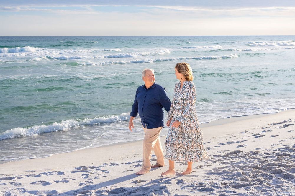 A couple walking hand in hand along a sunny beach with turquoise waves crashing on the shore.