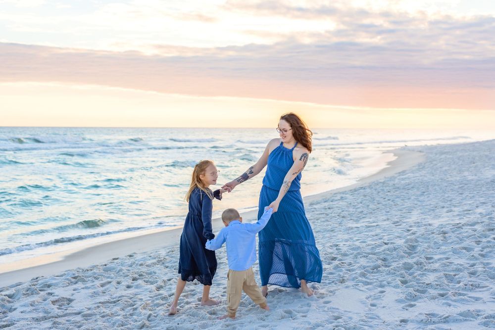 A family in blue outfits walks together along a white sandy beach at sunset creating a peaceful coastal scene.