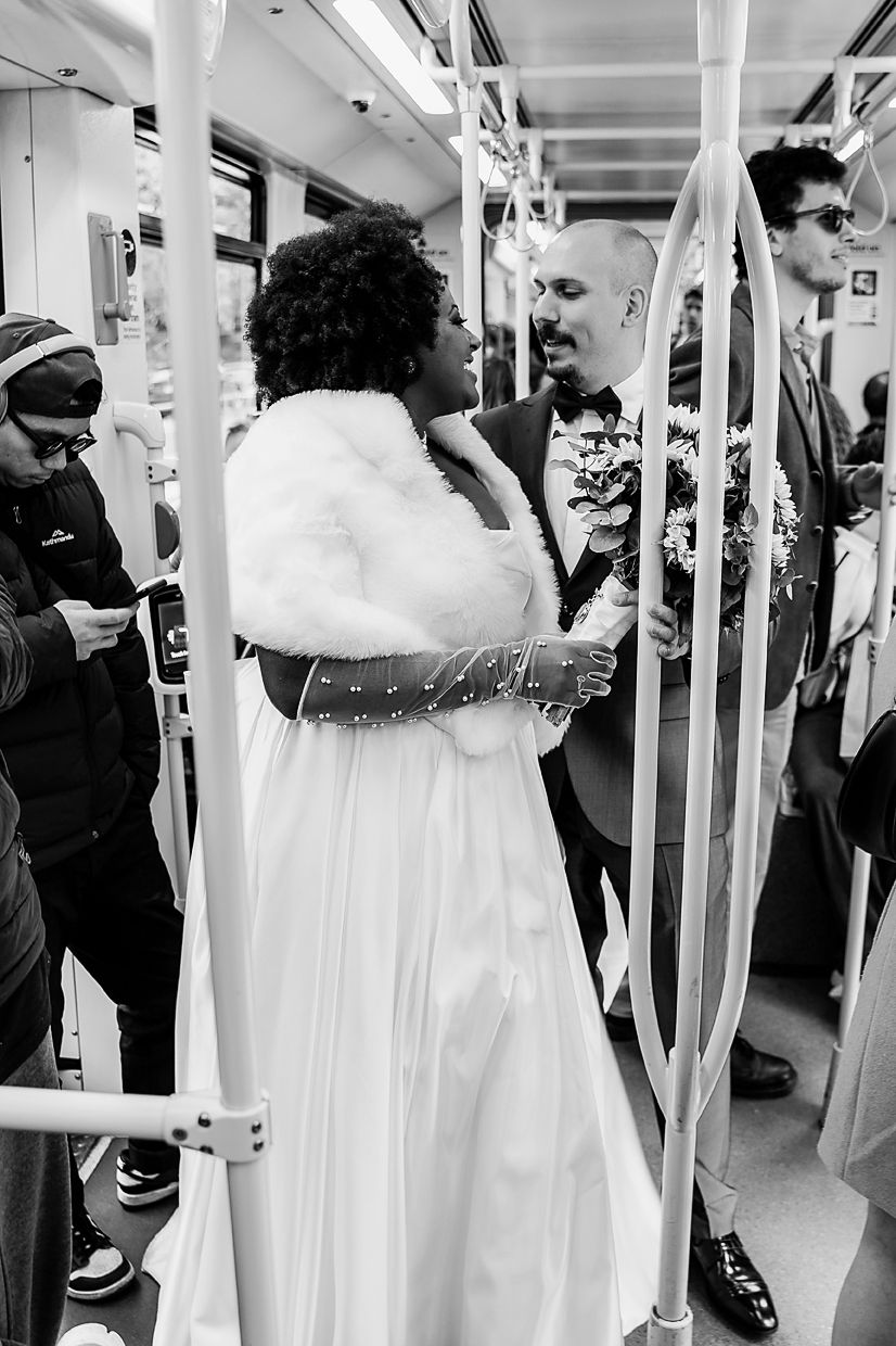 A wedding party riding on a subway train with people in white dresses and formal attire.