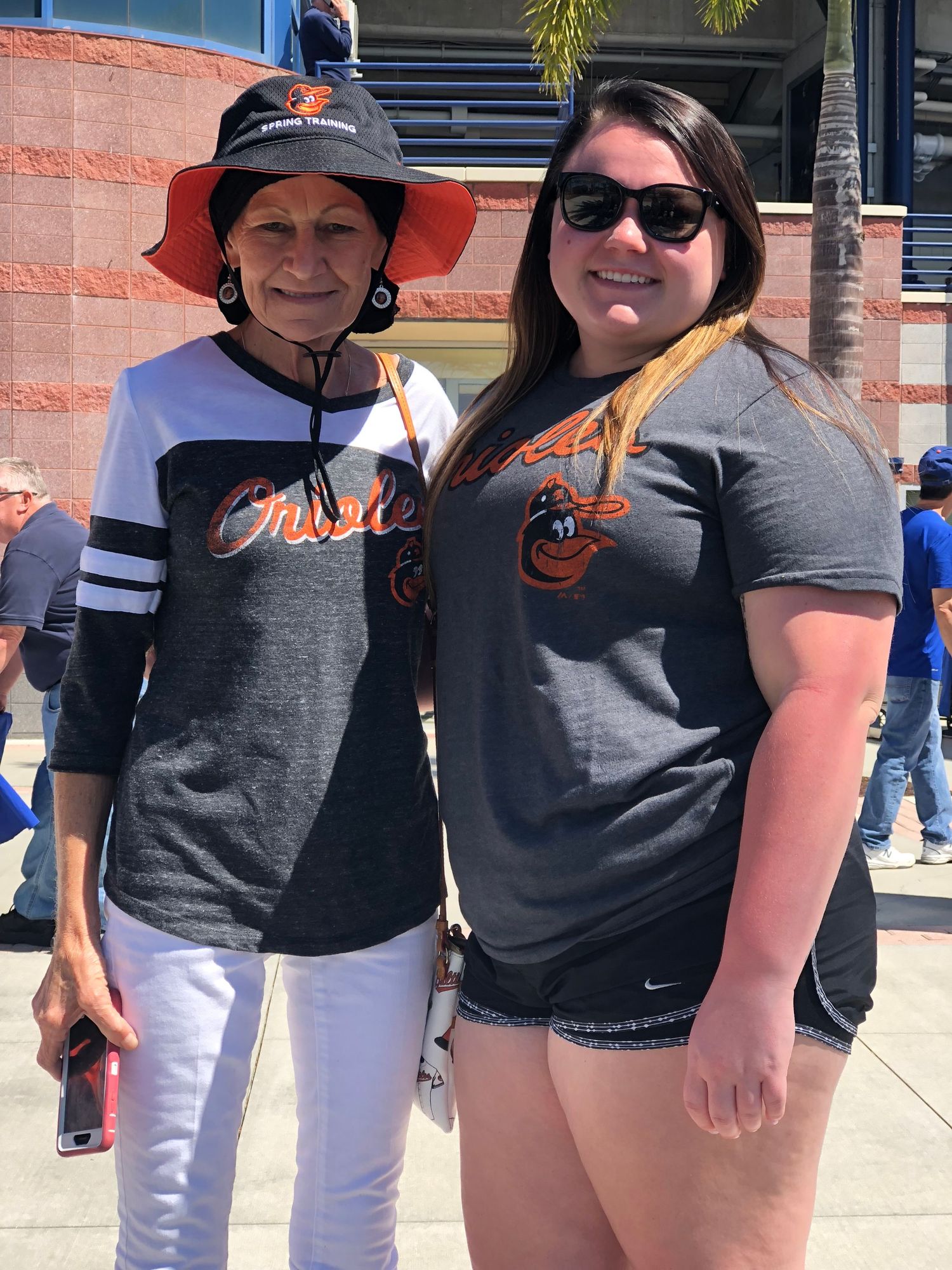 Baseball fans wearing team apparel and hats pose together outside a stadium on a sunny day.