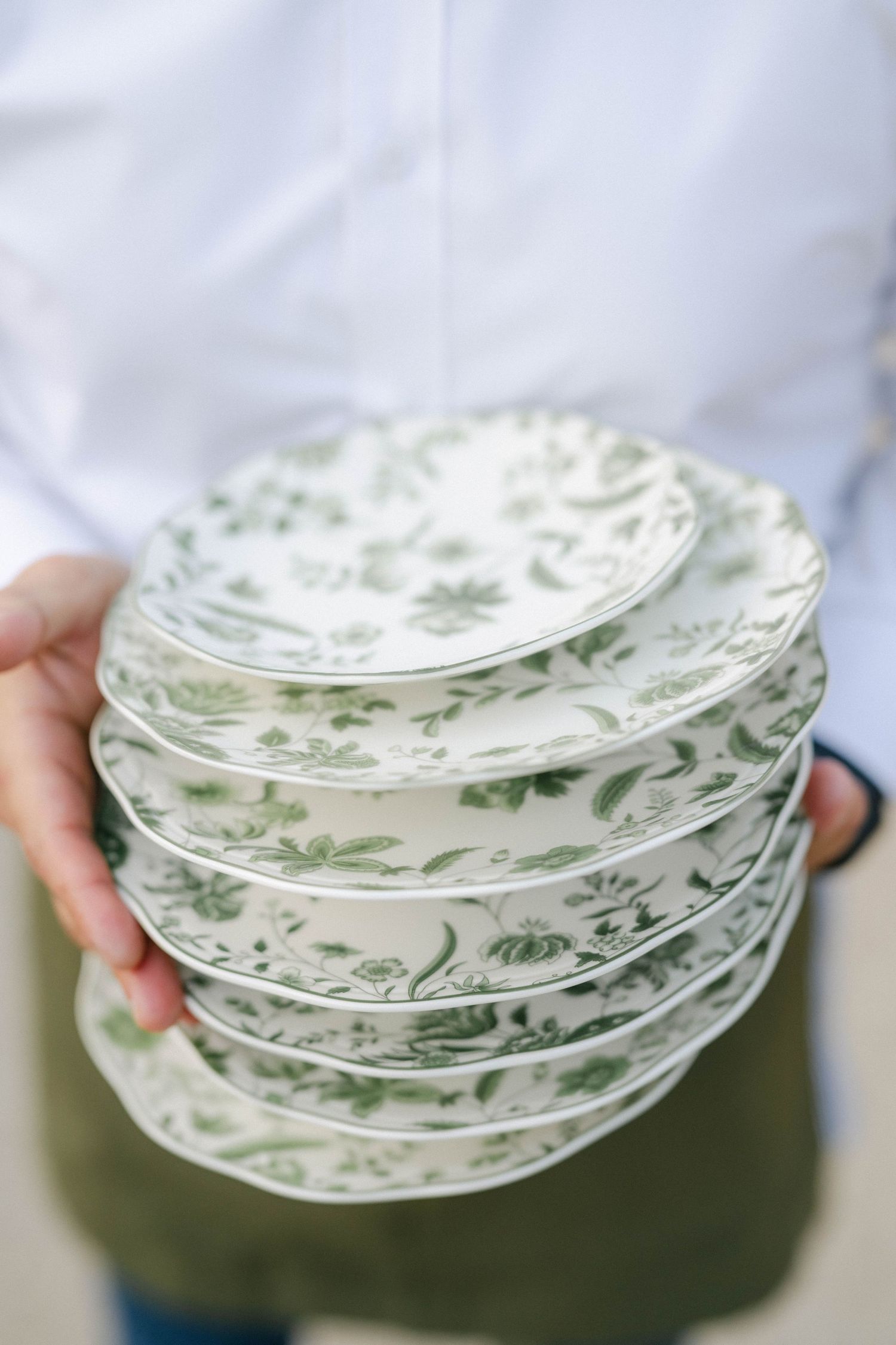Stack of vintage green and white floral patterned plates held against a light background. - Elawa Farm
