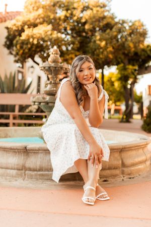 White patterned dress and sandals by stone fountain during golden hour.