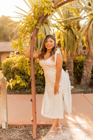 White floral dress against palm trees and yellow foliage in garden setting.