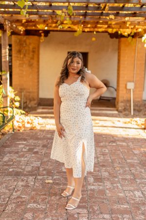 Floral white midi dress with side slit under pergola with string lights.