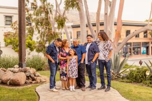 Family group photo outdoors with palm trees and Spanish architecture in the background.