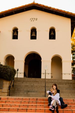 Historic Spanish mission building dated 1772 with couple seated on brick steps at entrance.