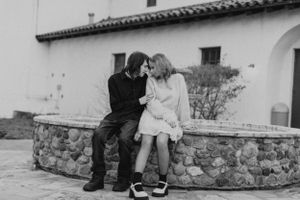 A romantic black and white photo of two people sitting close together on a stone wall.
