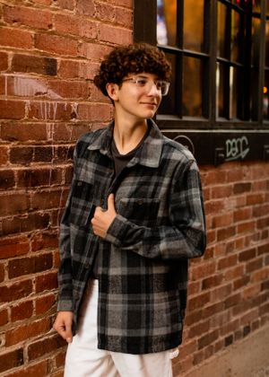 A casual portrait against a brick wall featuring someone in a plaid flannel jacket.