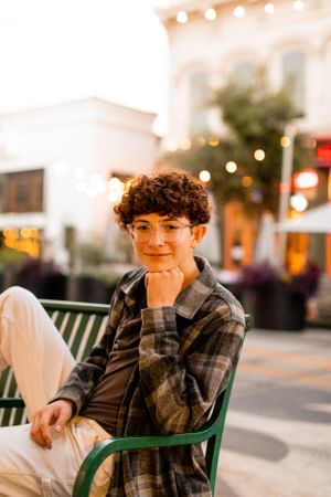 Outdoor portrait at dusk with string lights and urban scenery in the background.