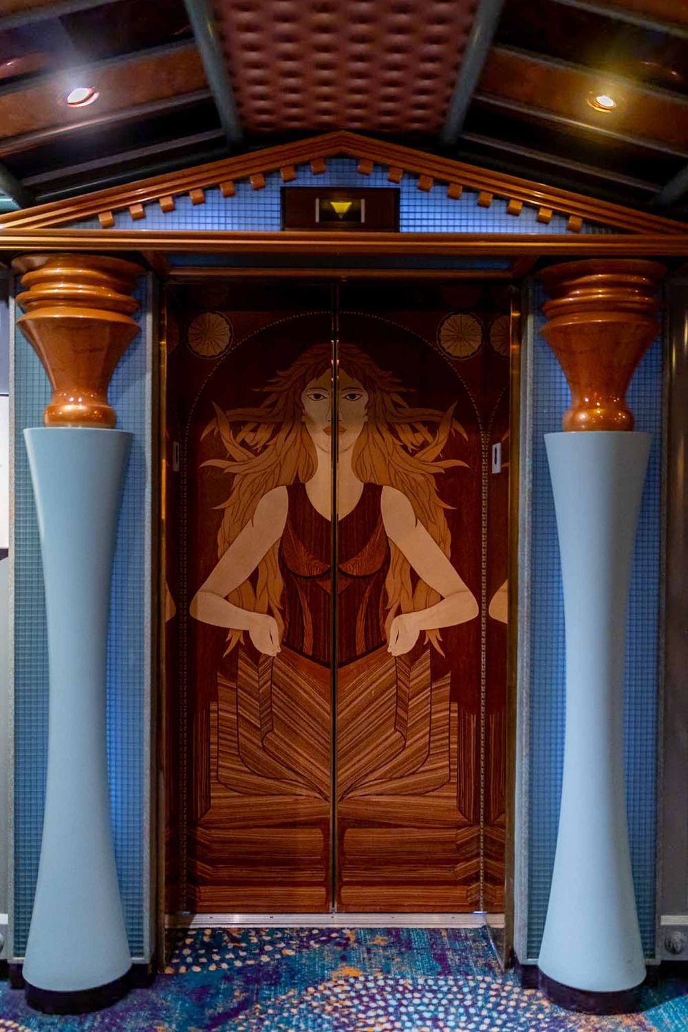 Art deco style wooden doors with geometric patterns and white columns create an elegant entrance in a modern building.