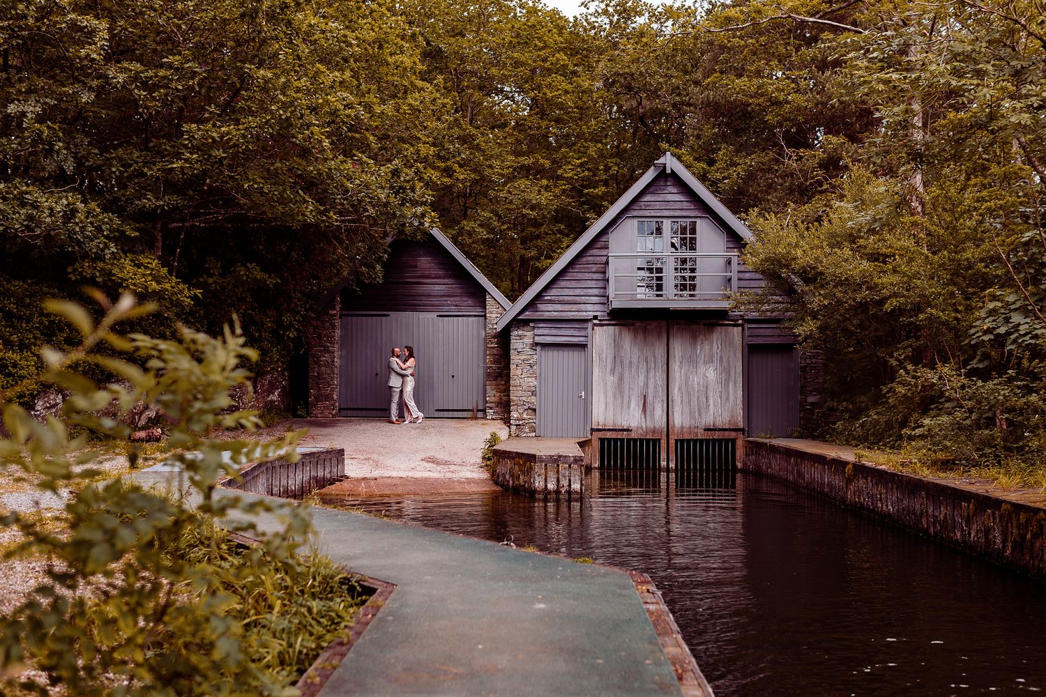 A series of wooden boathouses line a tranquil lake shore surrounded by autumn trees and foliage.