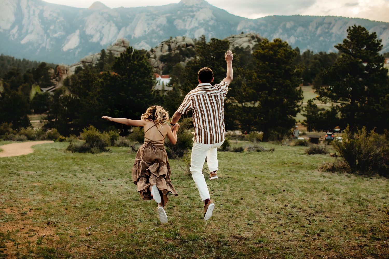 A couple walks through a scenic mountain meadow with their dog on a sunny afternoon.