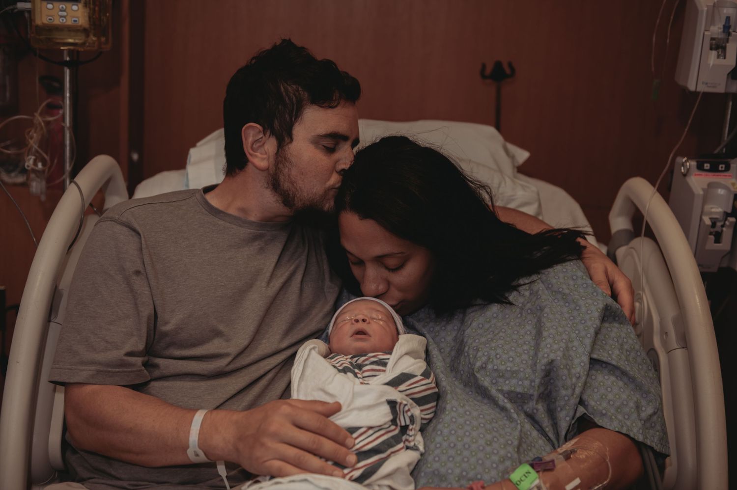 New parents sharing an intimate moment with their newborn baby in a hospital room.