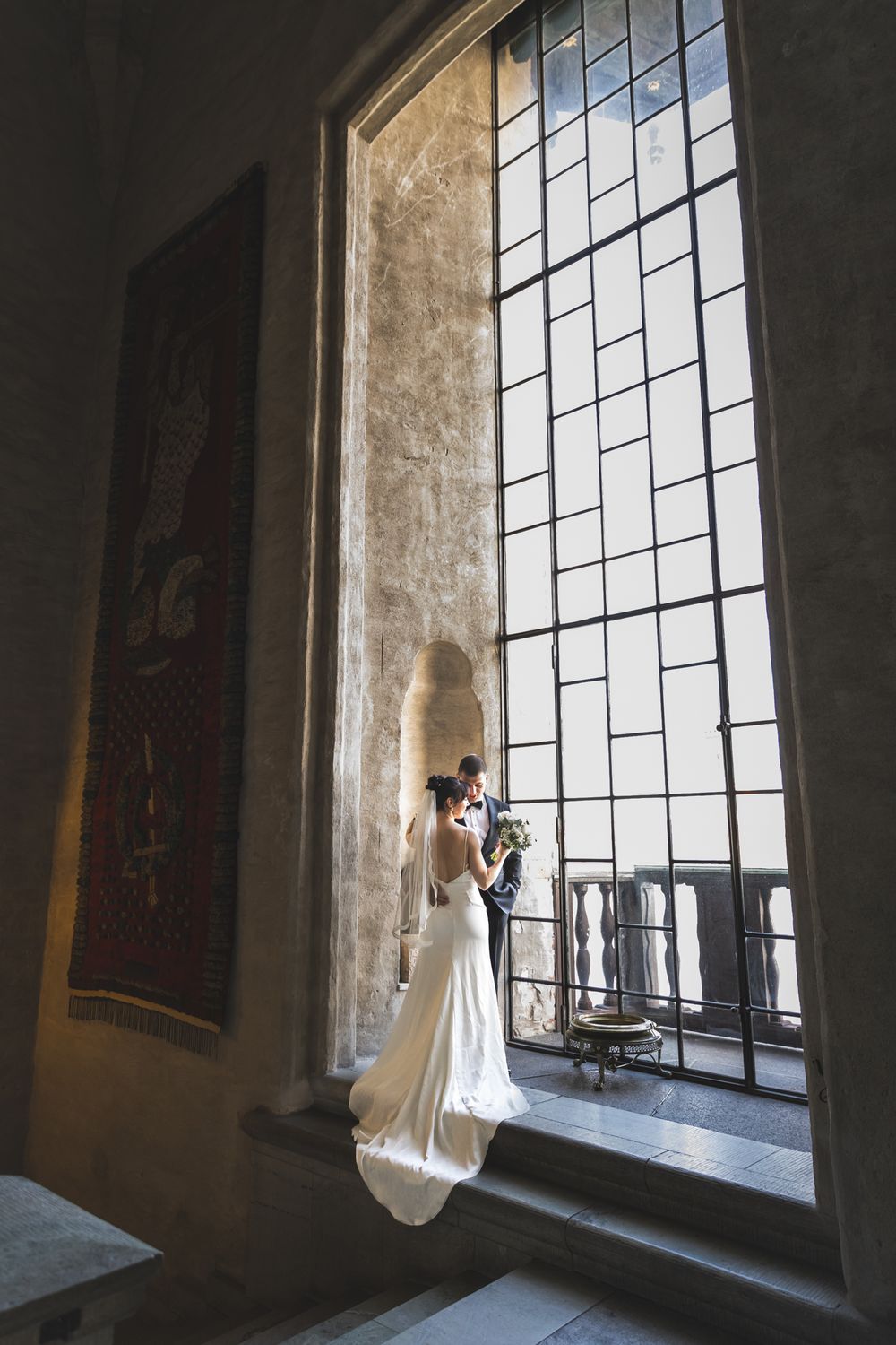 A bride in a flowing white dress stands silhouetted against a tall church window in a series of artistic wedding photos.