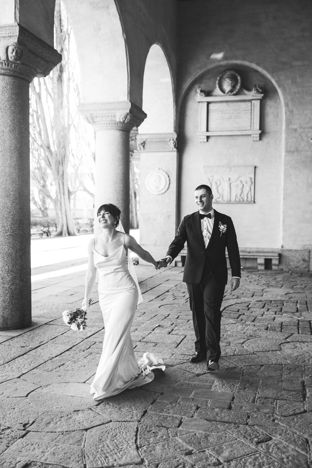 A couple walks hand in hand through an elegant stone archway corridor during their wedding celebration.
