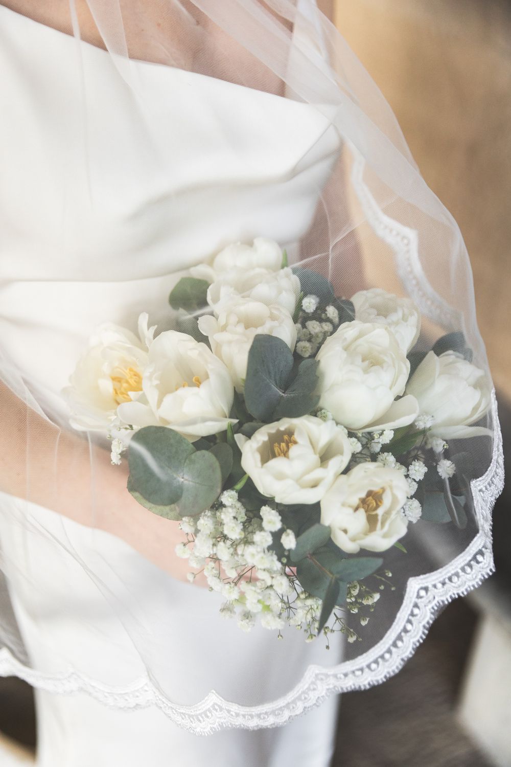 A delicate white wedding bouquet with eucalyptus leaves and baby's breath wrapped in lace-trimmed fabric.