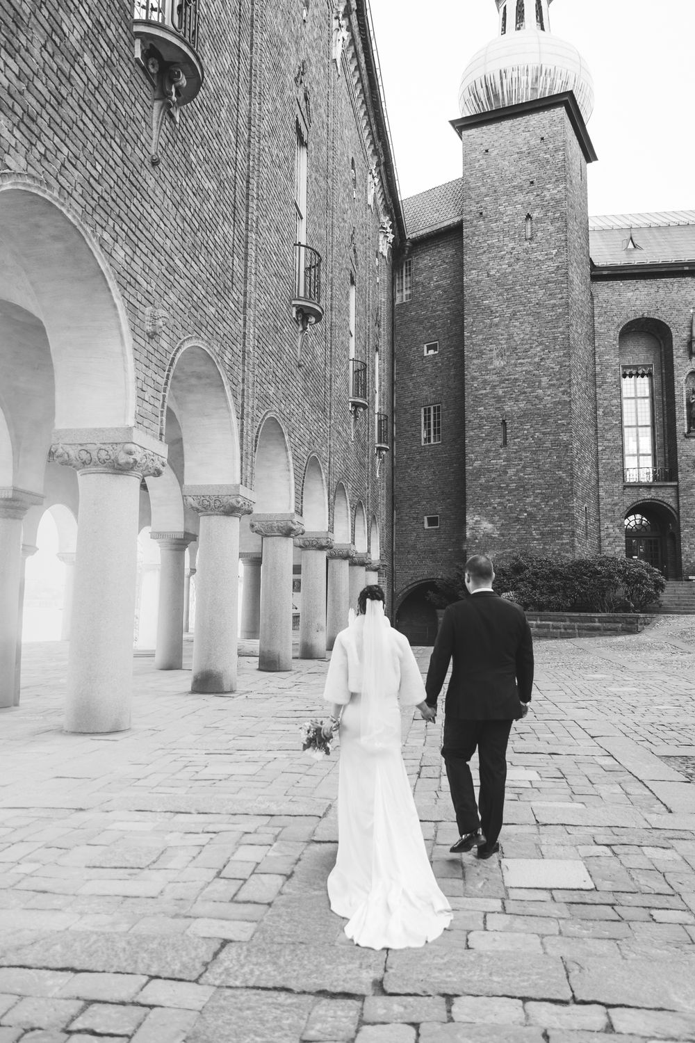 A series of black and white wedding photos showing a couple walking through an elegant arched colonnade.