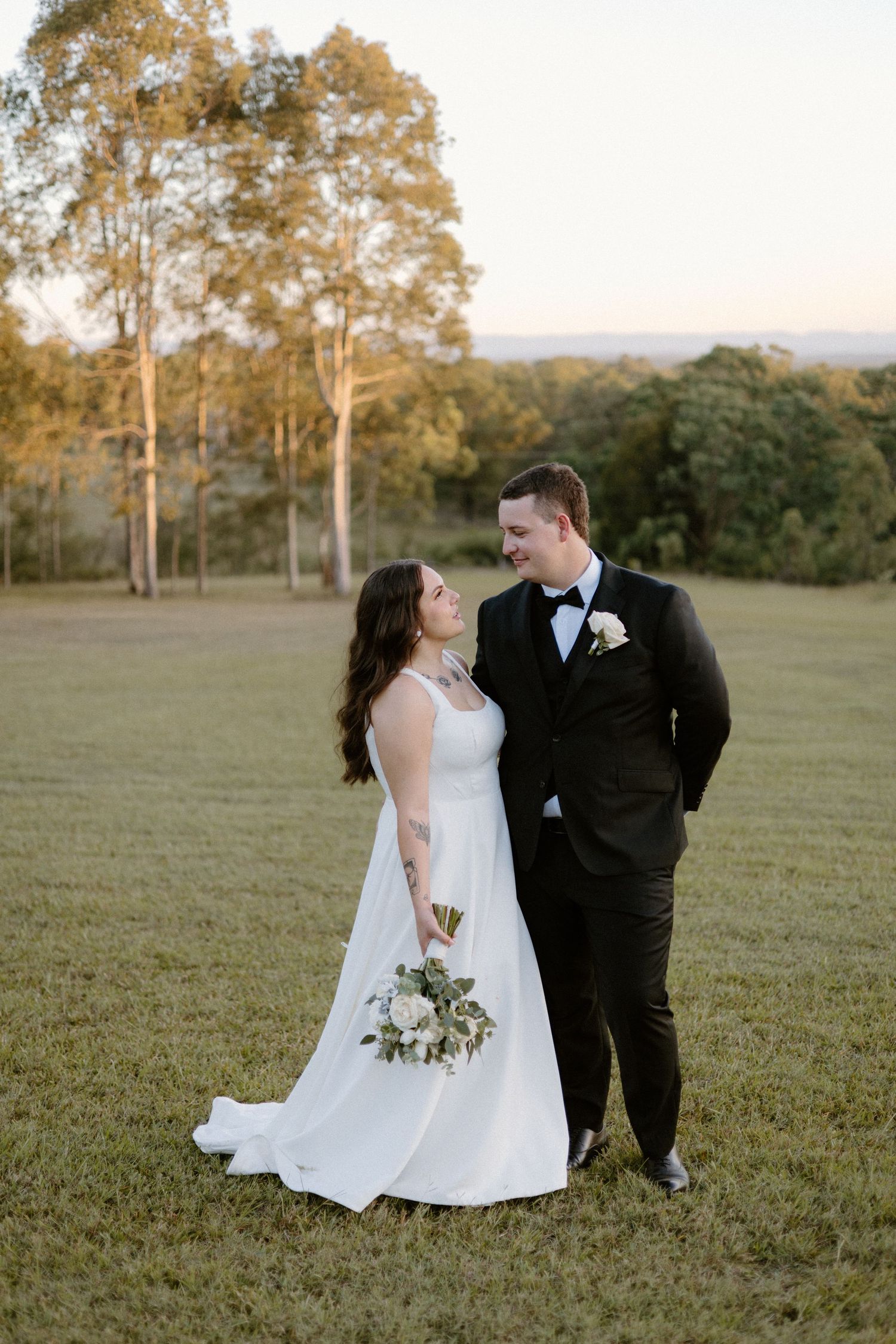 A romantic wedding couple shares intimate moments in a scenic field at sunset with eucalyptus trees in the background.