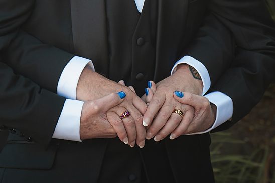 Close up of hands wearing wedding rings showing blue nail polish and formal attire during a ceremony.