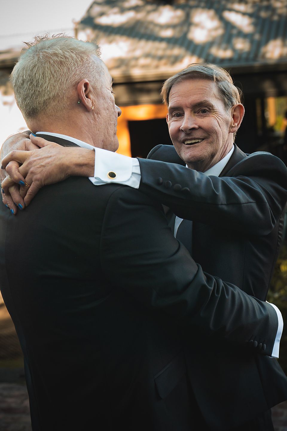 Two men in dark suits embrace warmly during what appears to be a formal event.