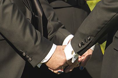 Close-up view of hands adjusting a formal black suit jacket sleeve at the wrist.