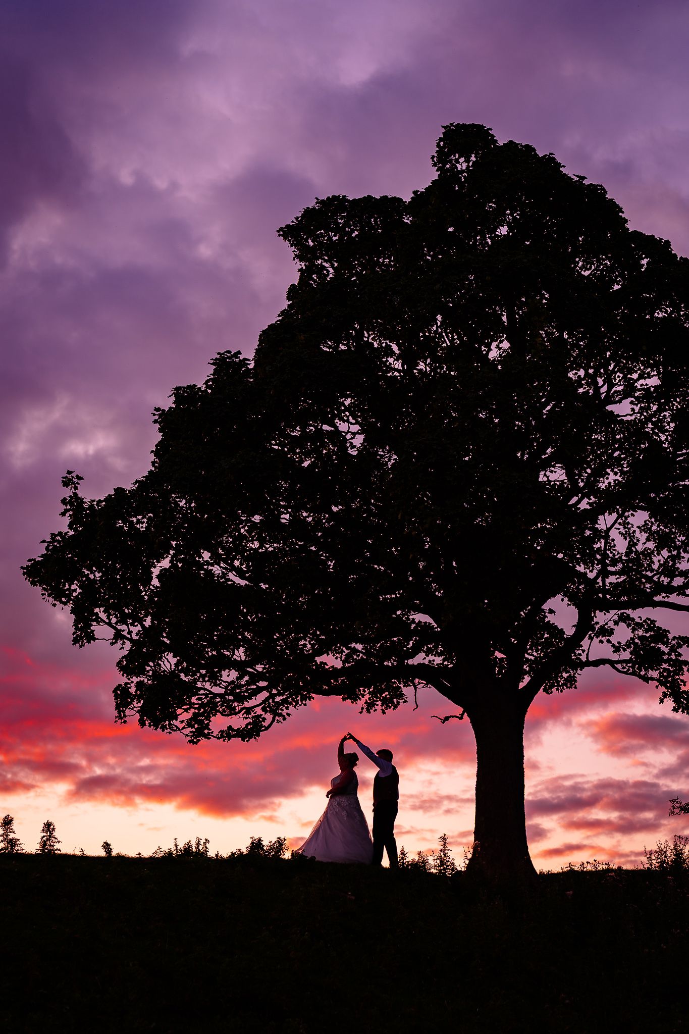 Silhouettes of a couple and trees against a dramatic purple and pink sunset sky.