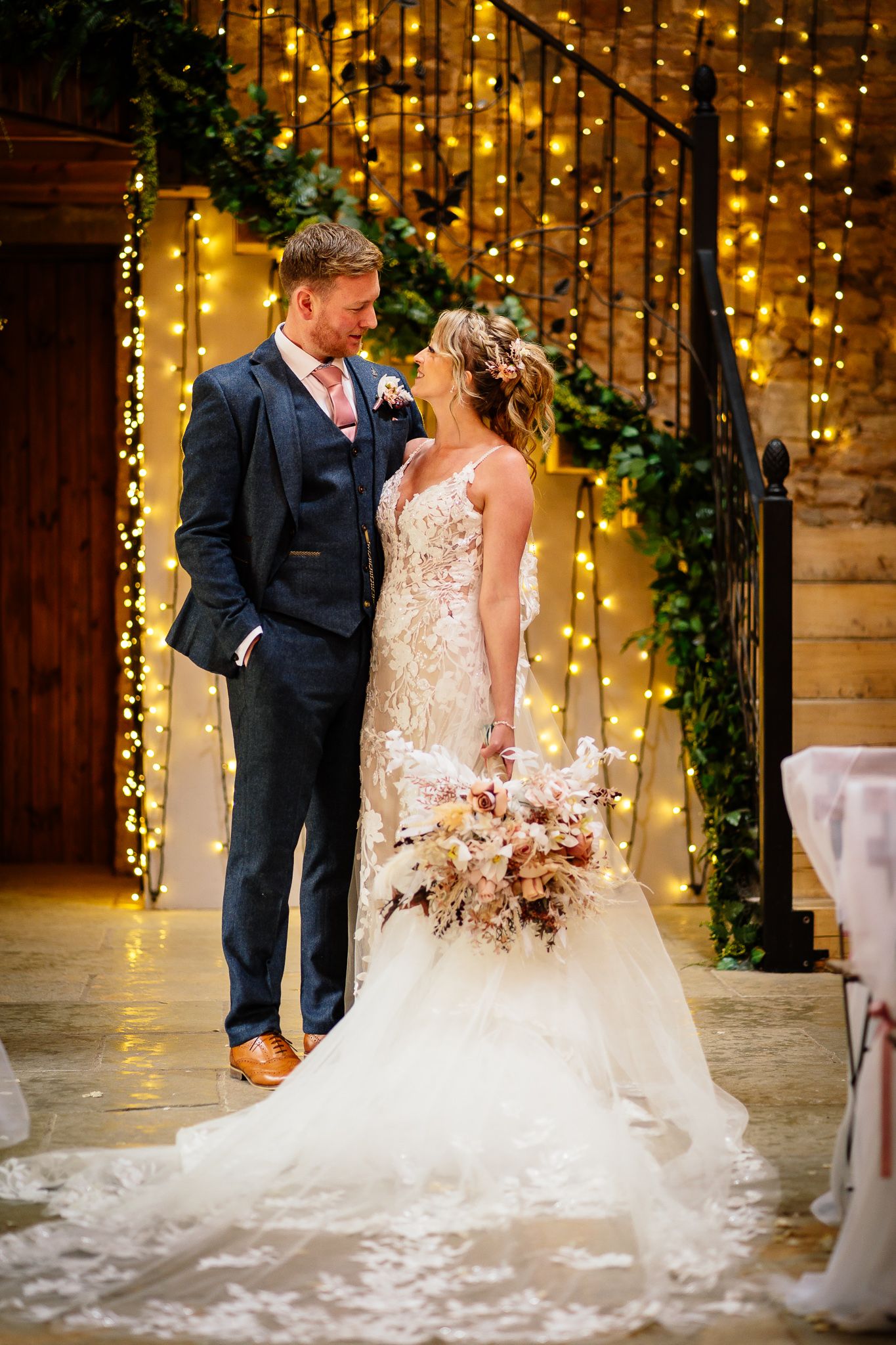 Wedding couple posing under romantic string lights against rustic backdrop.
