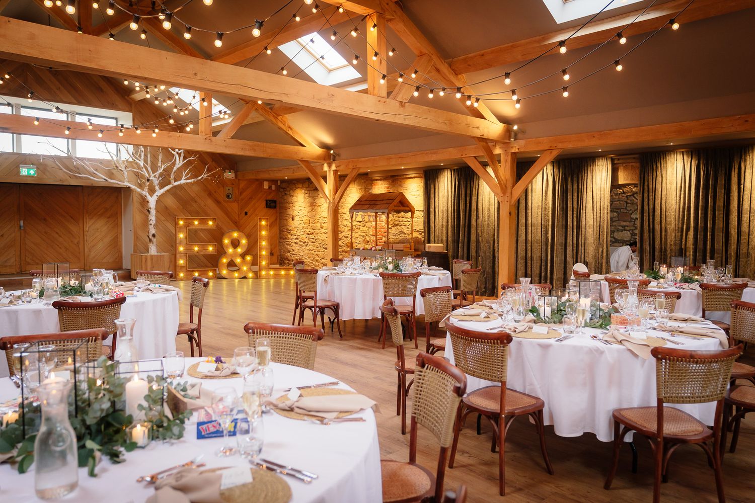 Elegant wedding reception venue with string lights and white table settings in a rustic barn setting.