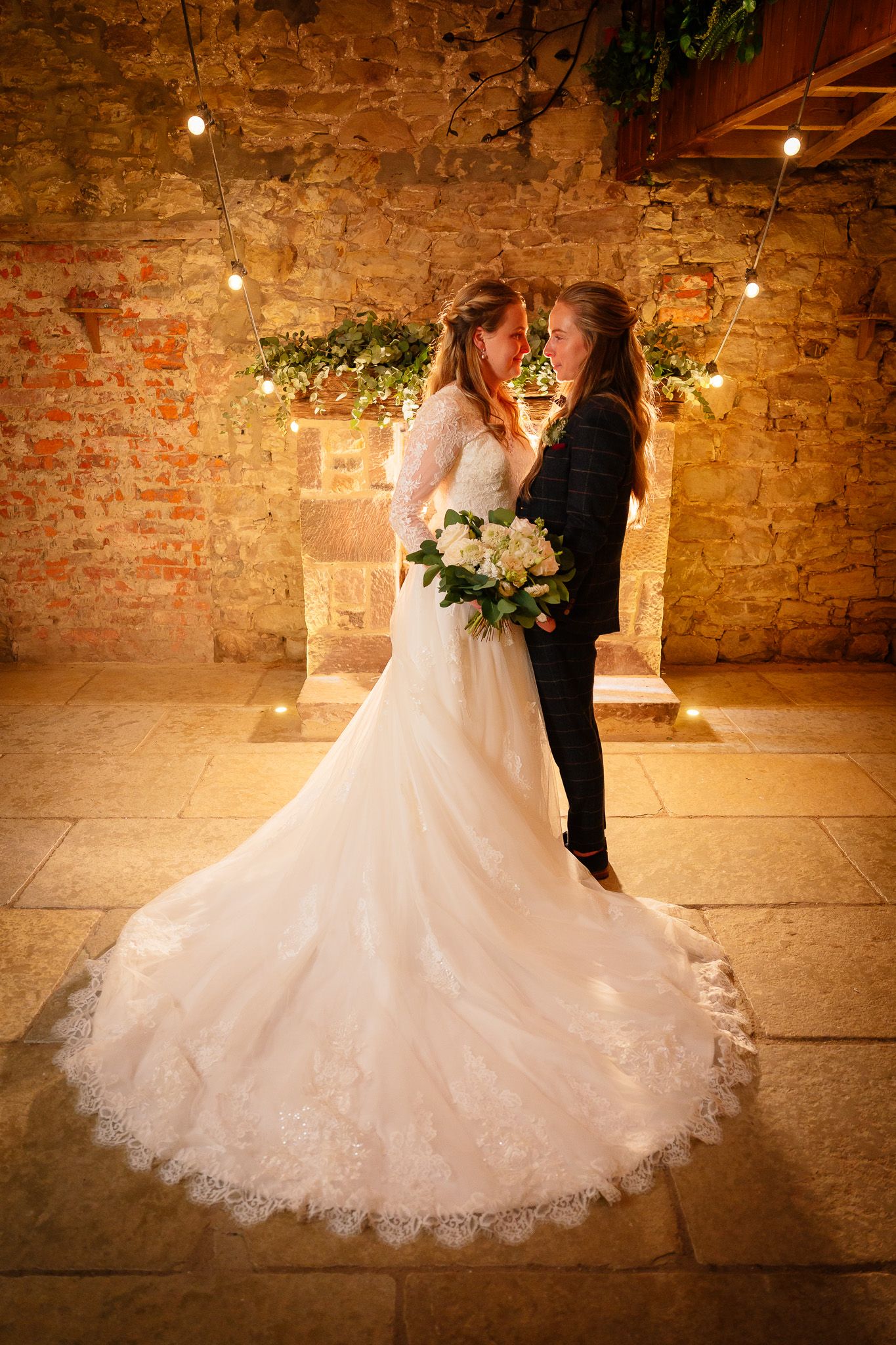 Beautiful wedding dress train spreads across rustic stone floor in romantic venue lighting.